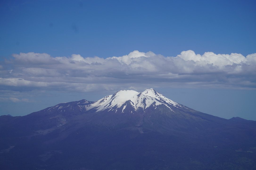 Un volcán nevado que se alza sobre una franja de nubes