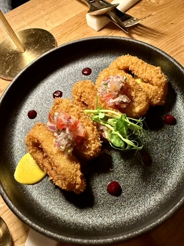 Crispy fried rings topped with salsa and microgreens on a dark plate
