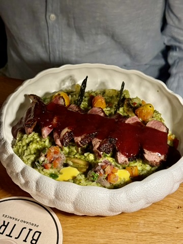 Sliced meat in a dark sauce over green rice in a white bowl
