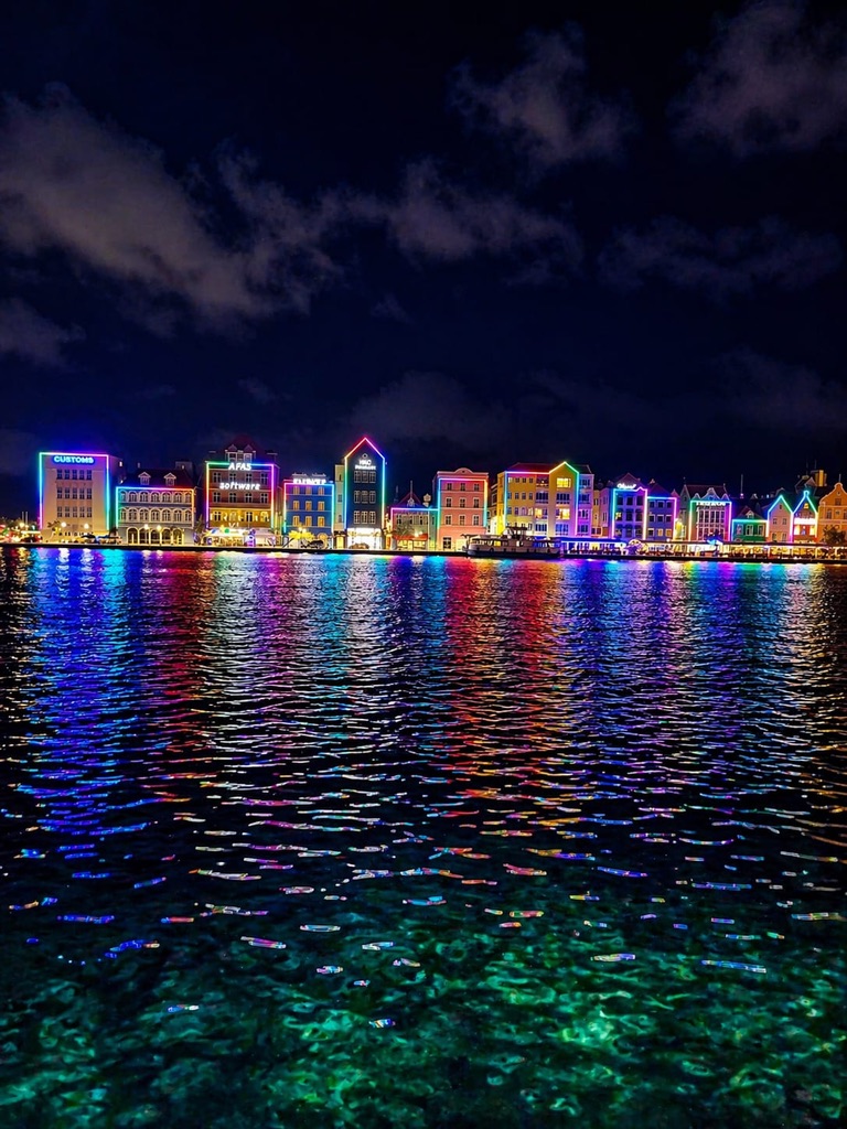 The colourful buildings of Willemstad’s Handelskade lit in neon at night, reflected in the water