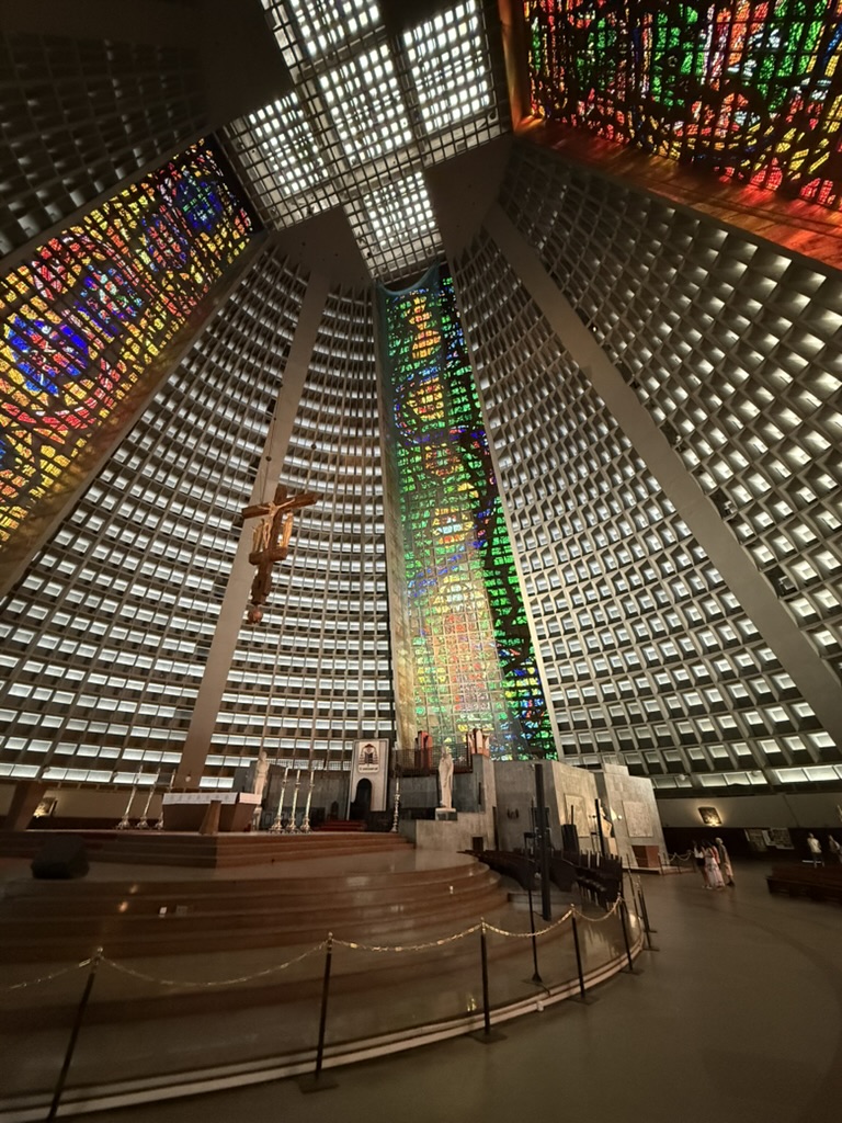 Inside the concrete cone of Rio's cathedral: tall stained-glass windows in red, yellow and green rise between walls of square openings to a glass cross
