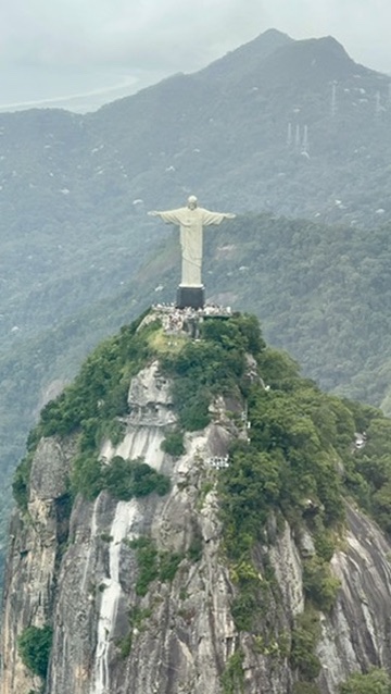 The statue of Christ the Redeemer with outstretched arms on the forested granite peak of Corcovado