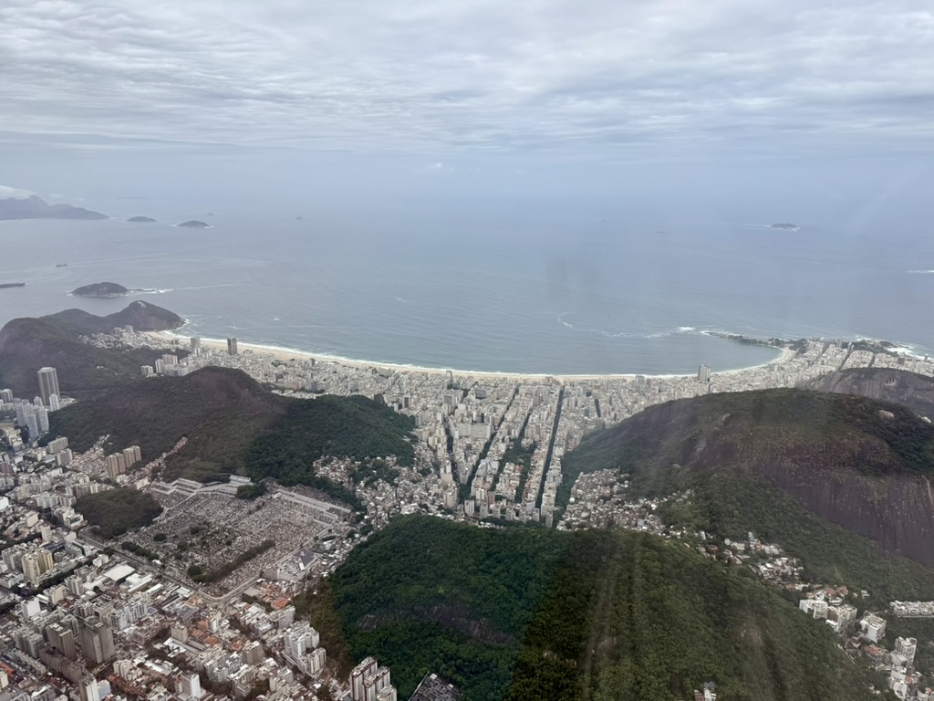Aerial view over green hills and dense city blocks to the long curve of Copacabana beach and the Atlantic