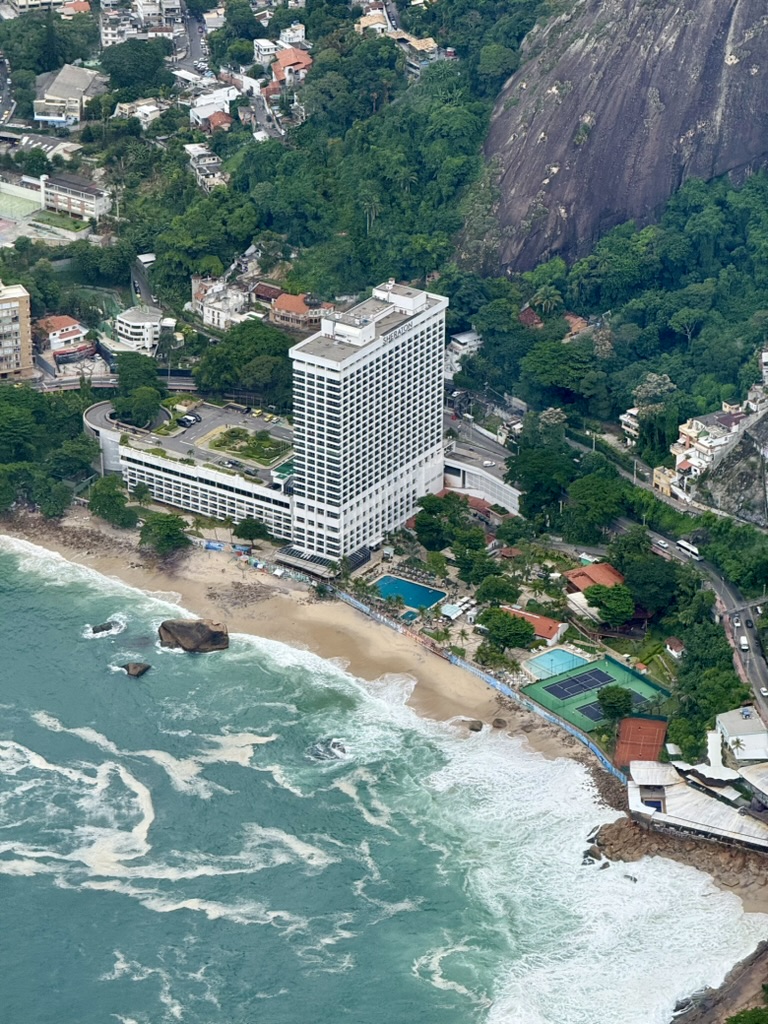 Aerial view of the Sheraton Grand tower with its pool, tennis courts and beach below a steep rock face