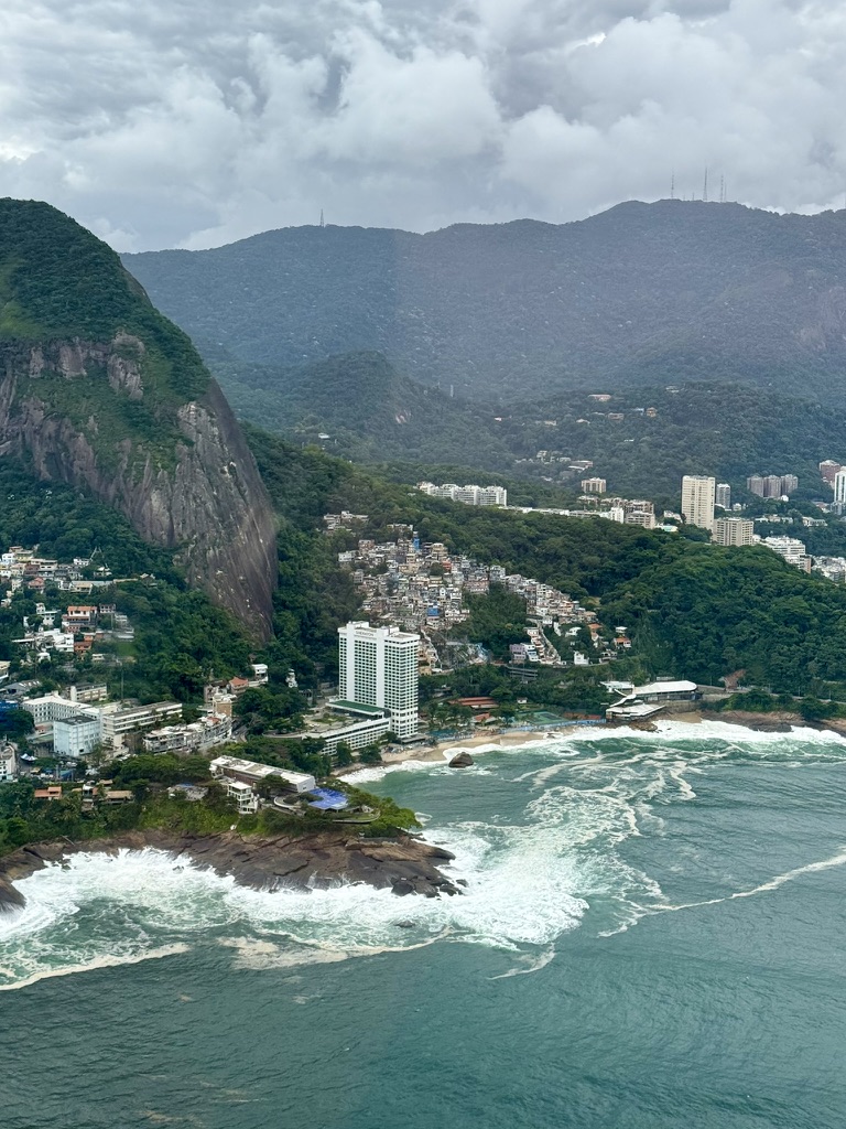 Aerial view of the Vidigal hillside and the rock face of Dois Irmãos, the white Sheraton Grand tower above a beach with rough surf