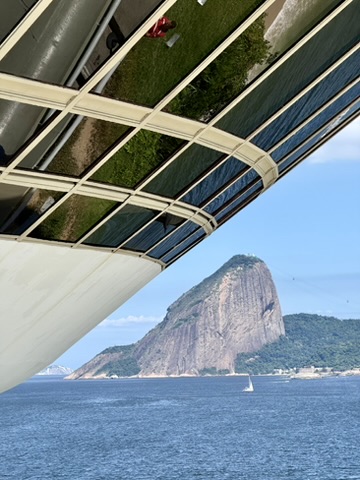 Sugarloaf Mountain across the blue bay, seen below the curved white rim and window band of the museum, a sailboat on the water