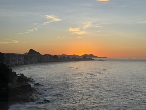 Sunrise over the curve of Leblon and Ipanema beach, city and mountains in silhouette against an orange sky