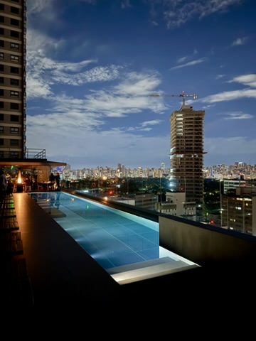 A long illuminated rooftop pool along the edge of a roof at night, towers and a construction crane beyond