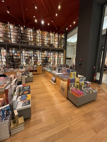 A bookshop with a red ceiling, a two-storey wall of shelves and low tables of books on a wooden floor