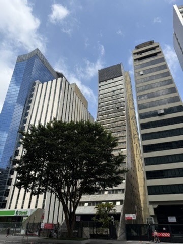 Three office towers, one glass, one white, one beige, above a tree on an empty Avenida Paulista