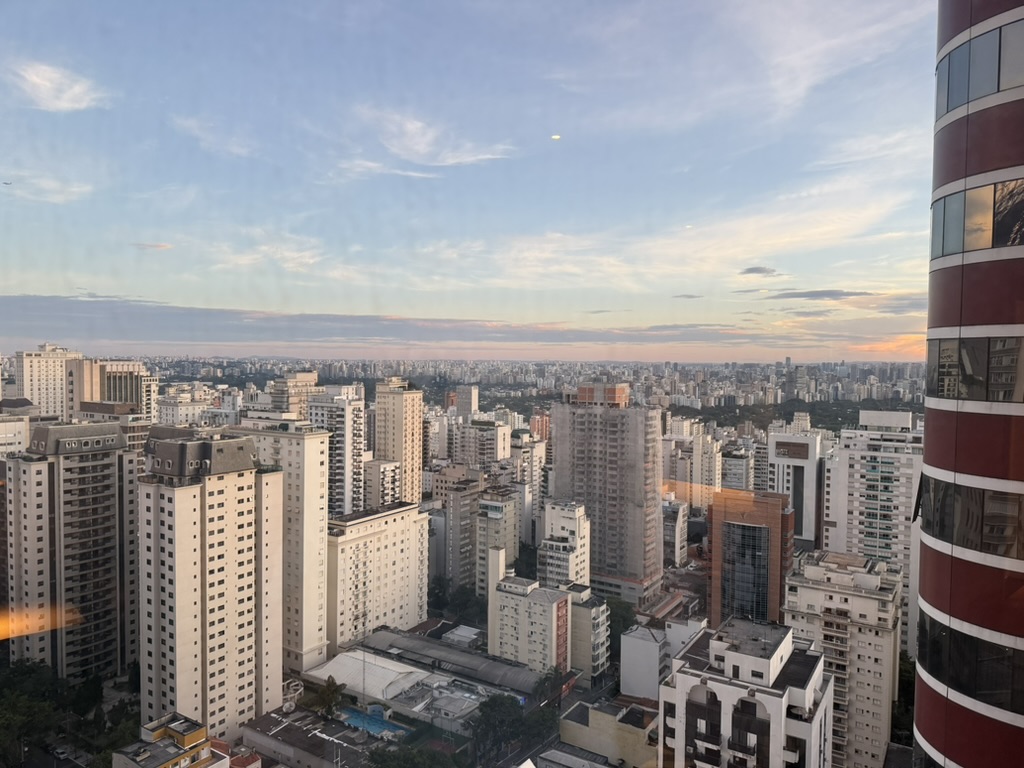 View from a high floor over the towers of Jardins at sunset, the maroon curve of the hotel's own tower on the right