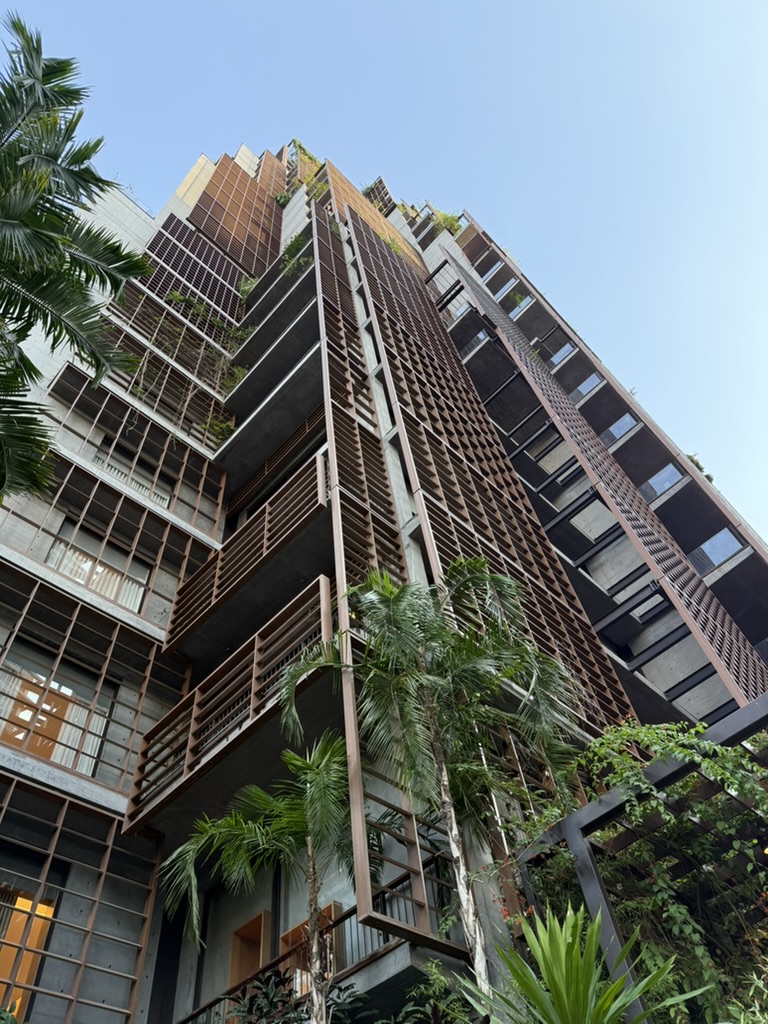 Looking up the Rosewood’s tower: wooden shutters, planted balconies and concrete, palms in the foreground against a blue sky