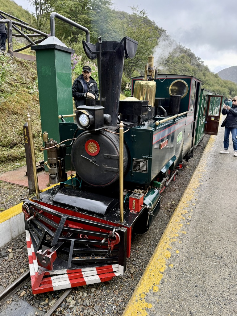 A small green steam locomotive at the platform of the End of the World Train in Ushuaia, steam rising