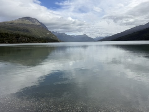 A long, still lake reflecting the clouds, mountains on both shores running away into the distance
